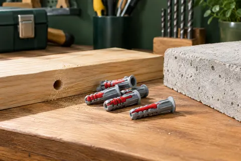 Chevilles de fixation gris et rouge posées près d’un perçage dans le bois et le béton