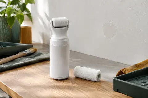 Petit flacon de peinture blanche mate avec rouleau intégré et rouleau de rechange, posé devant un mur intérieur